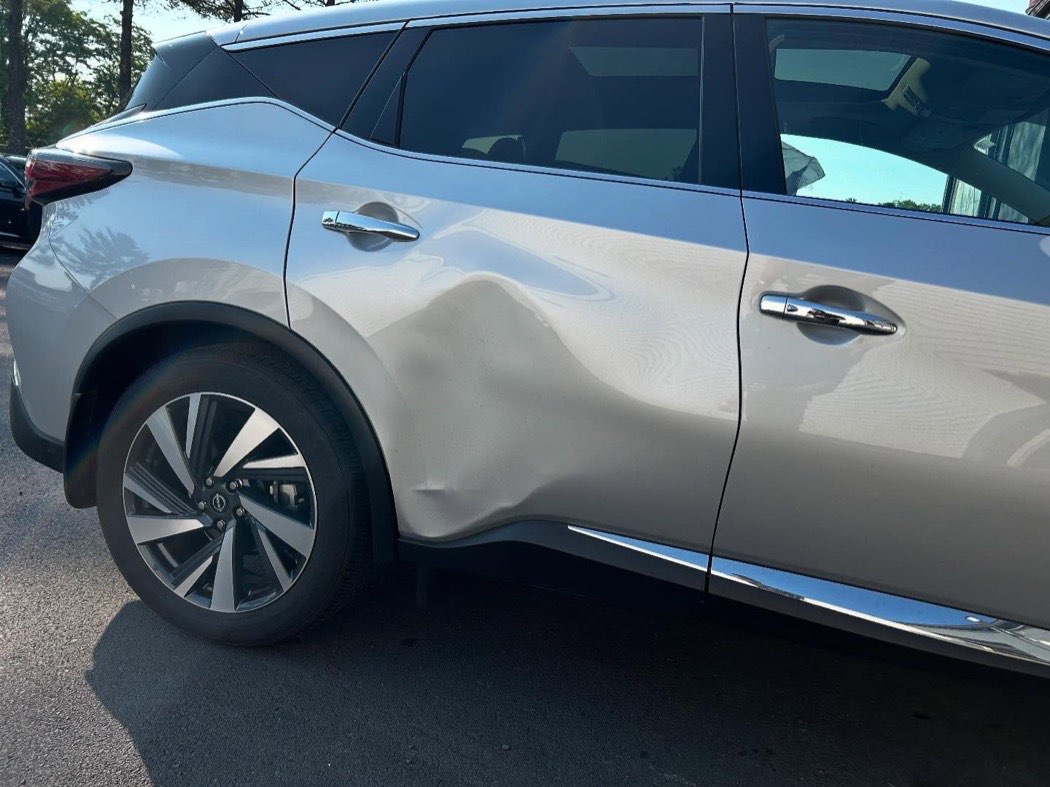 Close-up of a silver Nissan Murano with a deep crease running across the rear door and quarter panel.