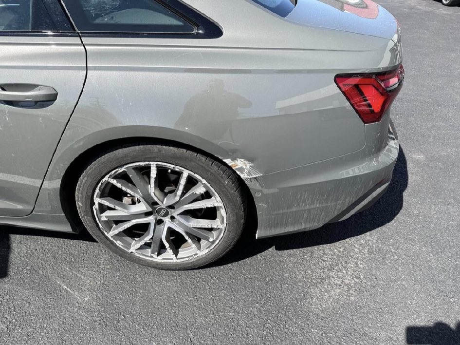 Gray Audi A6 with the rear bumper corner scraped and the rear wheel badly gouged.